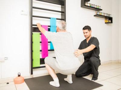 therapist assisting senior man doing squats in clinic